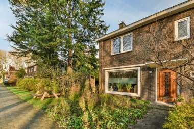 Amsterdam, Hollanda - 10 Nisan 2021: Ön bahçesinde ağaçlar ve çalılar olan bir evin dış görünüşü, arkasından alınan tuğladan bir patikadır.