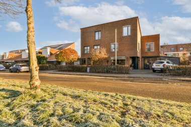 Yan tarafında arabaları olan bir cadde ve arka tarafında evleri olan tuğlalı binalar.