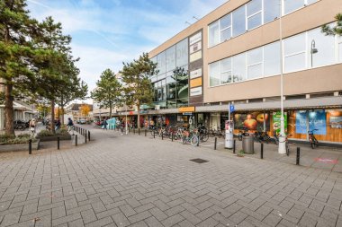 Amsterdam, Hollanda - 10 Nisan 2021: İnsanların yürüdüğü ve bisikletlerin yol kenarına park edildiği bir şehir caddesi, bir ofis binasının önünde.