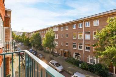 Amsterdam, Hollanda - 10 Nisan 2021: Sokakta arabaların park ettiği bir balkon ve arka planda apartman manzaralı binalar