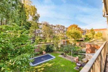 Önünde ağaçlar, çalılar ve çimenler olan bir arka bahçe. Görüntü bir apartmanın balkon penceresinden alınıyor.