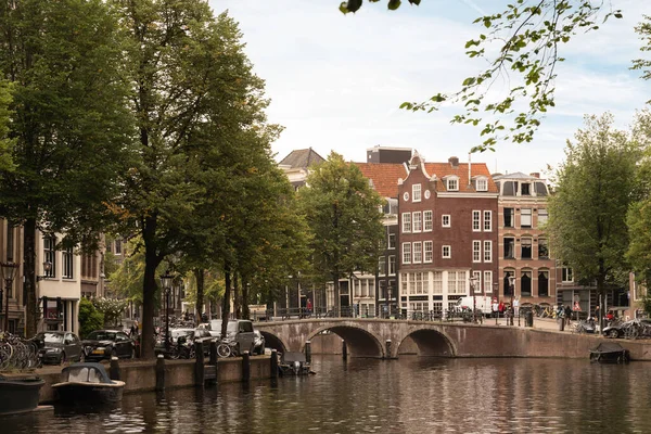 stock image Amsterdam, Netherlands - 10 April, 2021: a canal with boats and buildings in the background, as seen from across the water there are many trees on both sides