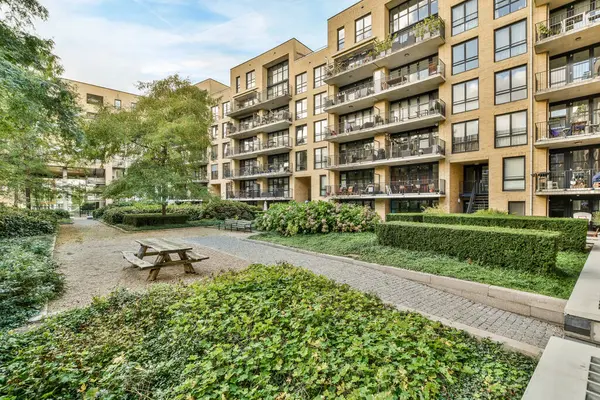 stock image Amsterdam, Netherlands - 10 April, 2021: an apartment complex with trees and bushes in the fore - sway area, including a bench that is surrounded by plants