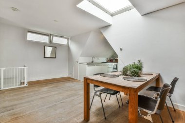 Tavanında uzun yıllardır kullanılmakta olan tavan pencereleri olan bir odada bir yemek masası ve sandalyeler.