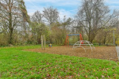 Amsterdam, Hollanda - 10 Nisan 2021: Parkta bir oyun alanı. Yerde yapraklar ve yanında ağaçlar, yukarıda mavi gökyüzü.