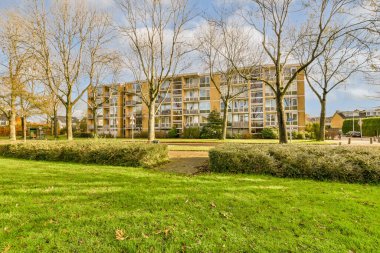 Amsterdam, Hollanda - 10 Nisan 2021: Ön planda ağaçlar ve yerde çalılar ve çalılarla çevrili yeşil çimenler olan bir apartman kompleksi