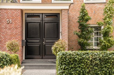 Amsterdam, Hollanda - 10 Nisan 2021: Girişin her iki tarafında yeşil bitkiler büyüyen kırmızı tuğla bir binanın önündeki siyah kapı