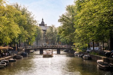 Amsterdam, Hollanda - 10 Nisan 2021: Nehrin karşısından görülebildiği üzere, su üzerinde tekneleri ve ağaçları olan bir kanal.