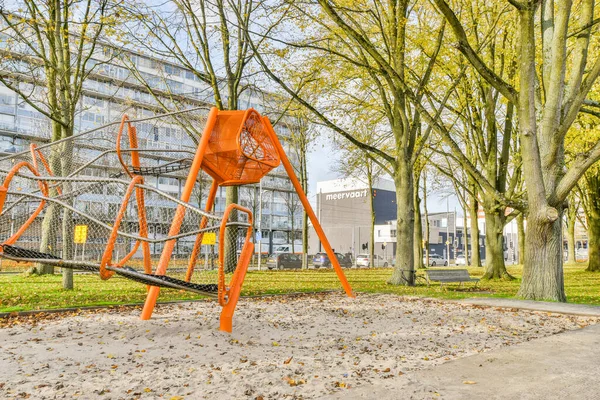 公园中央的橙色雕塑 地上有树叶 后面有建筑物 — 图库照片