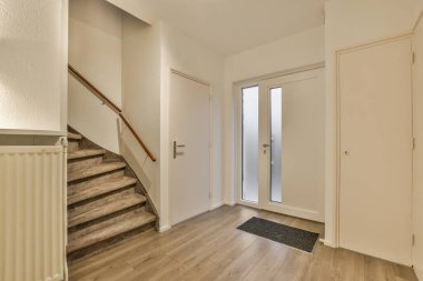 Ahşap döşemeleri ve beyaz duvarları olan boş bir oturma odası. Bu dairenin ikinci katına çıkan merdivenler.