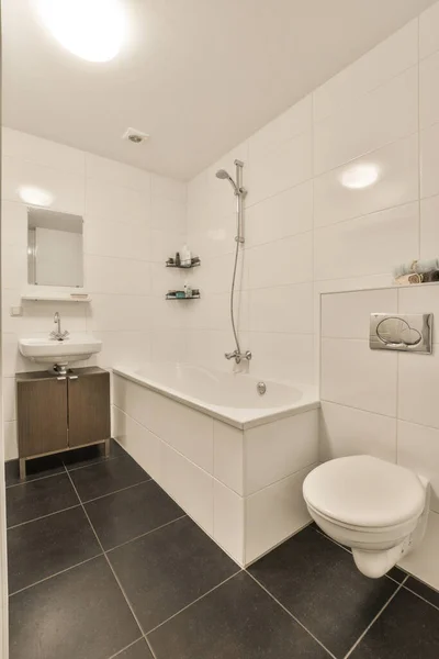 壁に黒いタイル張りの床と壁から壁までの白いバスルームにはシャワースタンドにトイレがあります — ストック写真