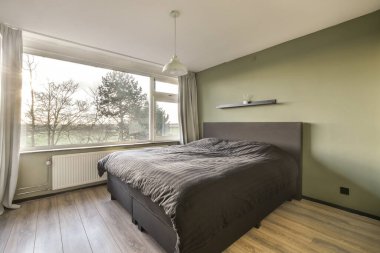 Ahşap döşemeli bir yatak odası ve ağaçlara bakan büyük bir pencere çok temiz.