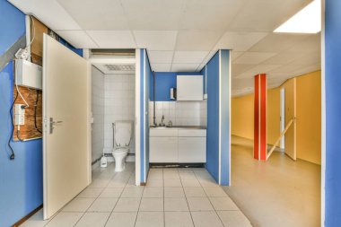 Boş bir banyo, mavi duvarlar ve yerde beyaz fayanslar, kapıdan tuvalete kadar görüldüğü gibi.