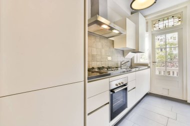 Beyaz dolapları olan bir mutfak odası ve duvarında fırın olan, verandaya çıkan bir kapının önünde.