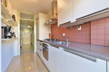 Duvarlarında kırmızı fayanslar ve tezgahın önünde ahşap döşemeler olan bir mutfak.