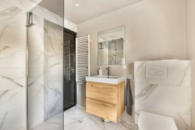 Mermer duvarları ve yerde beyaz fayansları olan modern bir banyo. Köşesinde duş kabini var.