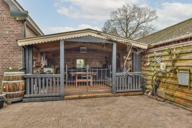 Güneşli bir günde evin arkasında tuğla ve ahşap çitlerle çevrili bir açık mutfak alanı.