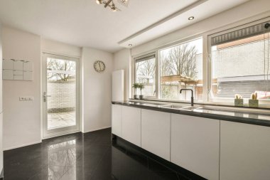 Pencerenin önünde beyaz dolapları ve siyah tezgahları olan bir mutfak. Dışarıdaki verandaya bakıyor.