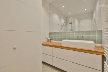 Lavabonun önünde beyaz dolapları ve ahşap tezgahları olan bir banyo seramik fayanslardan yapılmıştır.