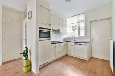 Ahşap döşemeli ve beyaz dolaplı bir mutfak tezgahın üstünde fırının önünde, lavabo ve bulaşık makinesi.