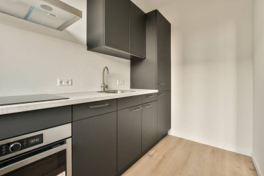 Modern bir mutfak, siyah dolapları ve beyaz tezgahları olan bir apartman dairesi.