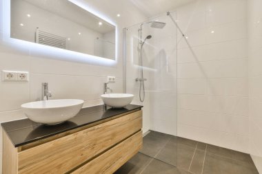 İki lavabosu ve arkasındaki duvarda büyük bir aynası olan bir banyo depo olarak kullanılan ahşap bir dolap.