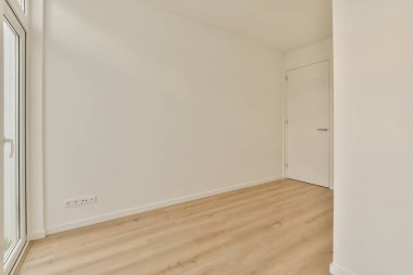 Beyaz duvarları ve sağında ahşap döşemeleri olan boş bir oda. Başka bir odaya açılan bir kapı var.