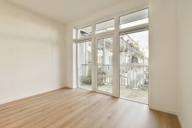 Ahşap zeminli boş bir oda ve evin önündeki terasa açılan sürgülü cam kapılar.