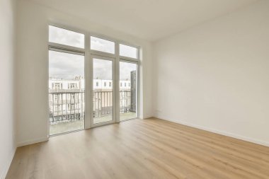 Boş bir oda, ahşap zeminli ve şehir haberleşmesine bakan cam kapılı.