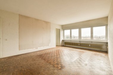 Boş bir oturma odası, ahşap döşeme ve duvarlarında beyaz boya, kimse yok.