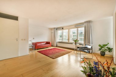 Odanın ortasında kırmızı deri bir kanepe ve ahşap zemin ve beyaz duvarlarla dolu bir oturma odası.