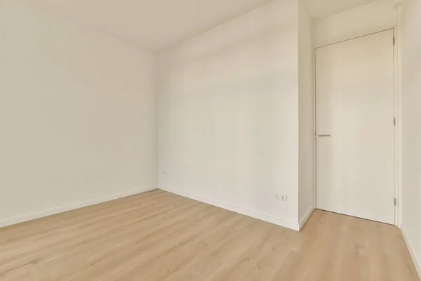 an empty room with white walls and wood flooring the door is open to reveal another room in the corner