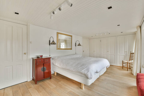 a bedroom with wood flooring and white walls, there is a red chair in the room next to the bed