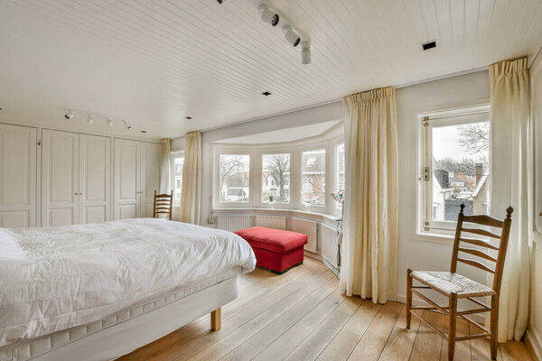 a bedroom with a bed, chair and window in the middle of the room that has white paint on the walls