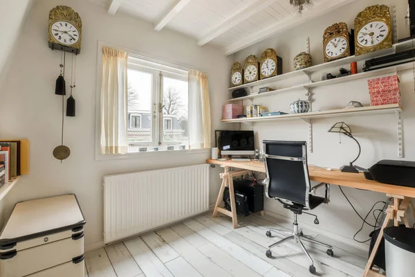 a home office with clocks on the wall and desk in front of window looking out onto an outside view