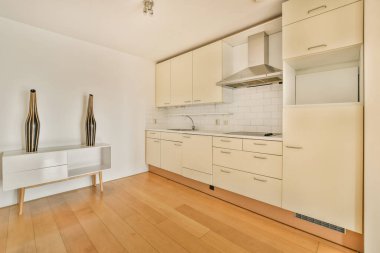 Odanın ortasında beyaz dolapları ve ahşap döşemeleri olan bir mutfak, sağ tarafında iki vazo var.