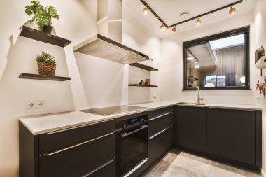 Modern bir mutfak, siyah dolaplar ve beyaz tezgahlarla, manzaraya açılan açık bir pencereyle birlikte.