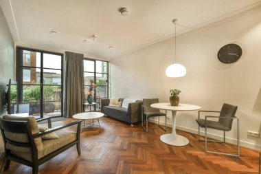 Ahşap zemini ve beyaz duvarları olan bir oturma odası. Sokağa bakan büyük bir pencere var.