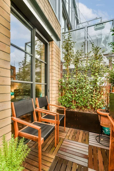 stock image two chairs on a wooden deck with plants in the foreground and an open door leading to a balcony area
