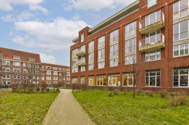 Binanın her iki tarafında da ağaçlar ve çalılar olan çimenli bir bölgenin ortasında bir tuğla bina var.