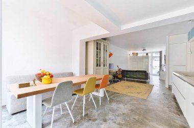 Masanın etrafında beyaz duvarlar, gri döşemeler ve açık renkli sandalyeler olan bir evde mutfak ve yemek odası.