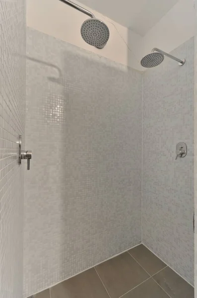 浴槽の前の壁にはシャワーヘッドと手が付いた白いタイル張りのバスルームがあり — ストック写真