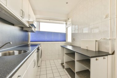 Bu fotoğraftaki tezgahların üzerinde beyaz dolaplar ve siyah tezgahlar olan bir mutfak alanı içeriden çekilmiş.