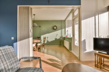 Duvarlarında mavi duvarlar ve beyaz süslemeler olan bir oturma odası. Başka bir odaya açılan açık bir kapı var.