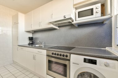 Bu fotoğraftaki tezgahların üzerinde beyaz dolaplar ve siyah tezgahlar olan küçük bir mutfak içeriden çekilmiş.