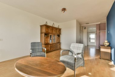 Ahşap döşemeleri ve beyaz duvarları olan bir oturma odası. İki mavi sandalyeyle çevrili ahşap bir sehpa da dahil.