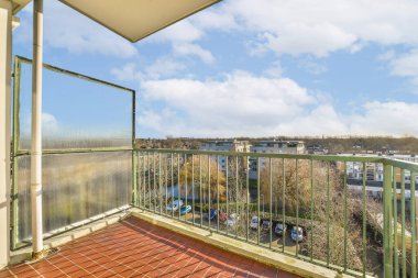 Yerde kırmızı fayanslı bir balkon ve mavi gökyüzünde beyaz bulutlar arkasında ise manzarası var.