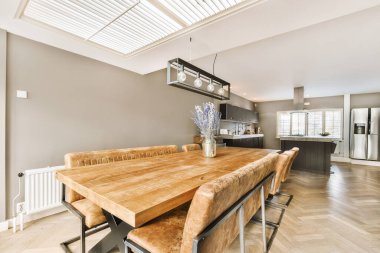 Ahşap masalı bir yemek odası ve üzerinde tavan penceresi olan açık mutfak alanının önünde sandalyeler.