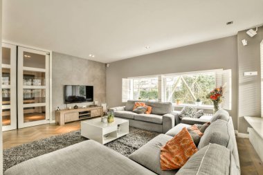 Gri kanepeleri ve beyaz kahve masası olan oturma odası turuncu yastıklarla süslenmiş.