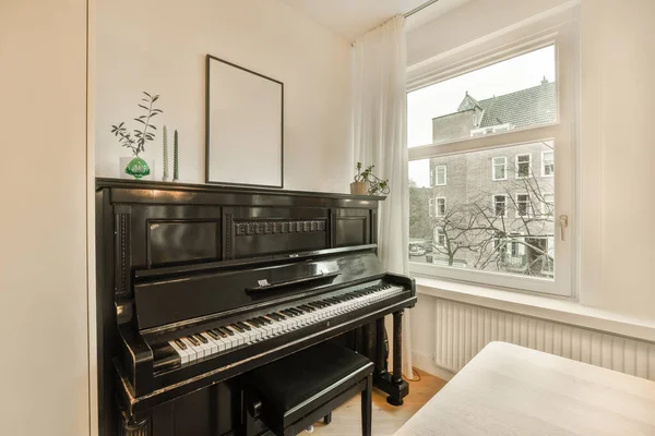 a piano in the corner of a room with a large window looking out onto an outside street and trees on the other side
